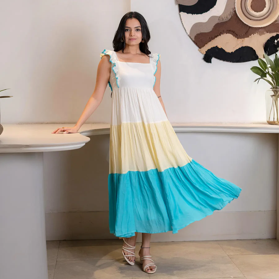 Woman in tiered white, yellow, and turquoise maxi dress posing indoors.