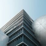 Modern architectural building with geometric glass facade and large metallic dome structure under clear blue sky