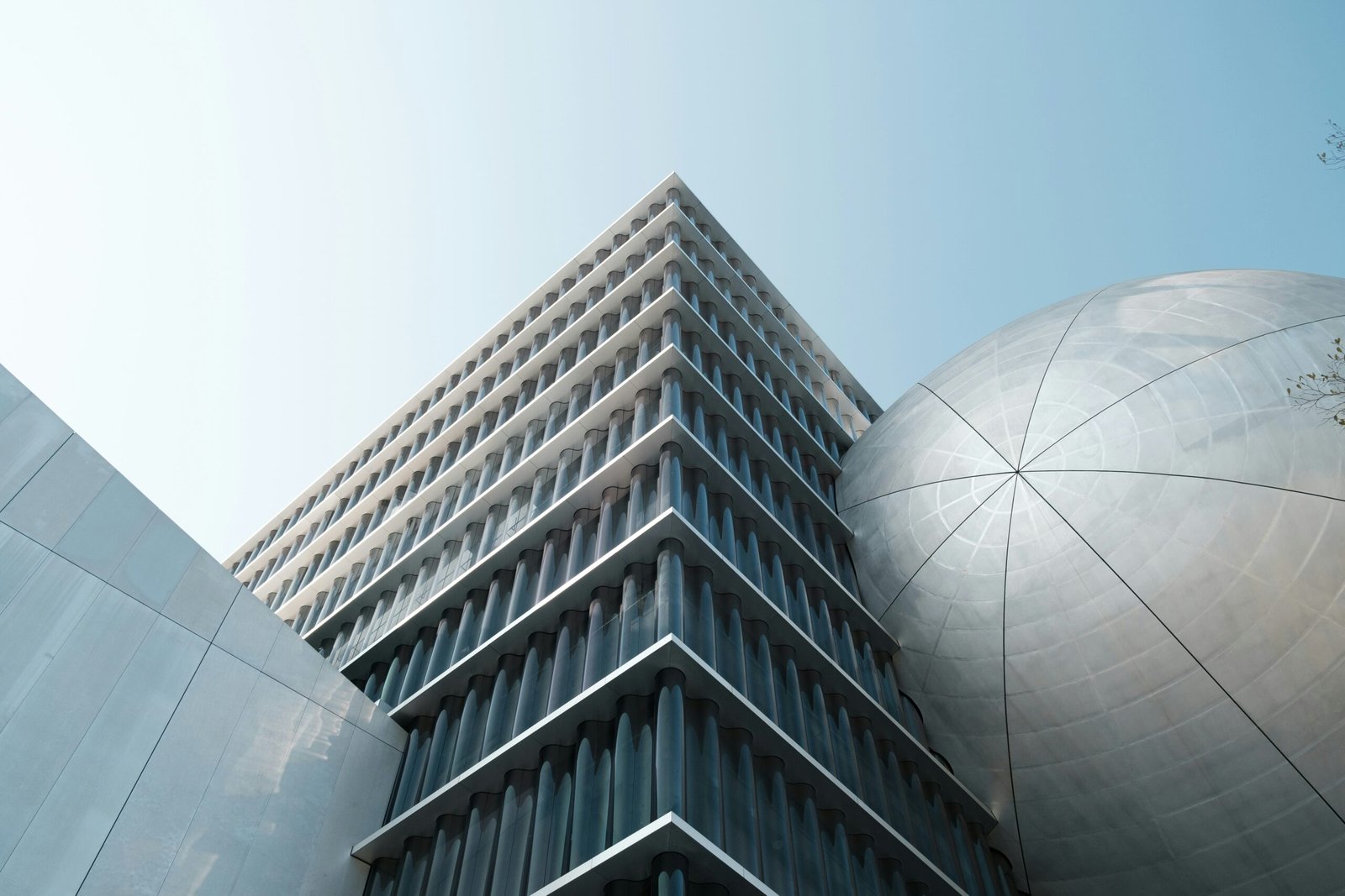 Modern architectural building with geometric glass facade and large metallic dome structure under clear blue sky